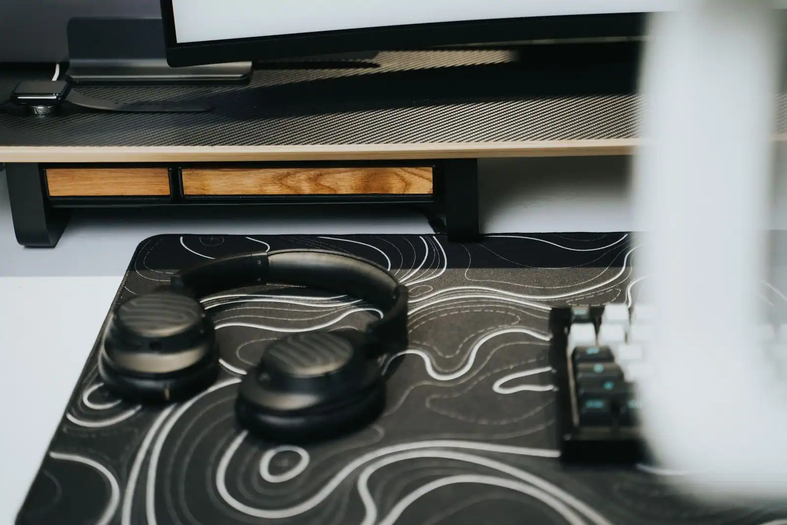 Bureau équipé d'accessoires informatiques : support d'écran, casque, clavier mécanique et tapis.