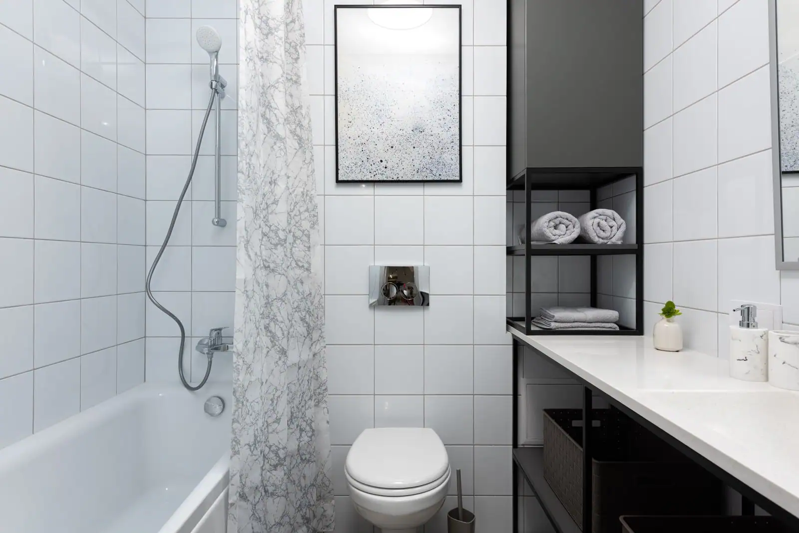 Salle de bain claire et carrelée avec étagères, serviettes pliées, distributeur de savon et panier