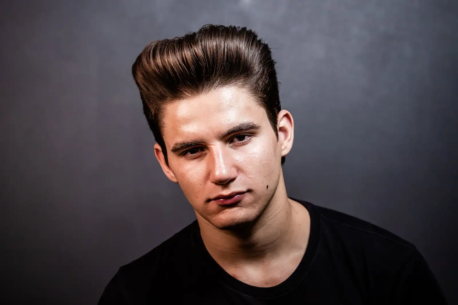 Portrait studio d'un jeune homme aux cheveux bruns lustrés et coiffés en arrière au produit coiffant