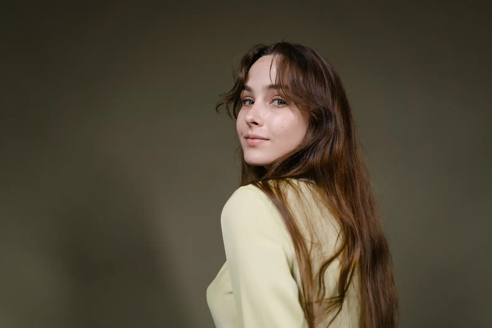 Femme aux longs cheveux bruns soyeux retombant sur l'épaule, portrait studio sur fond neutre