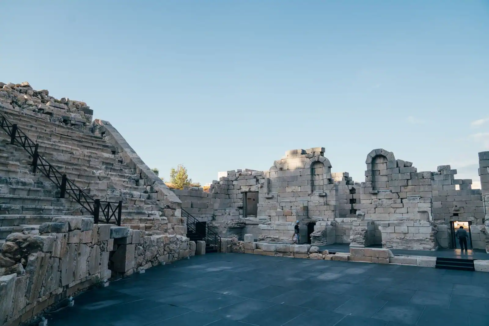 Gradins en pierre et mur de scène d'un théâtre romain antique, sous un ciel de fin de journée