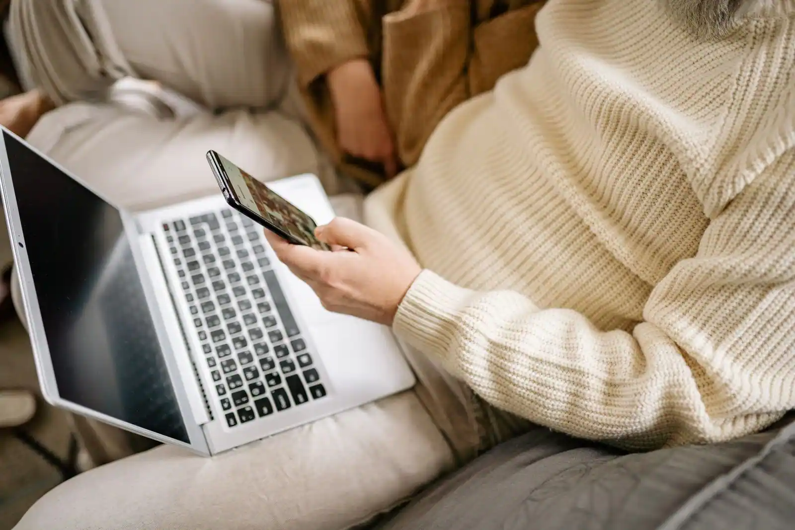 Personne utilisant un ordinateur portable et un smartphone, installée sur un canapé