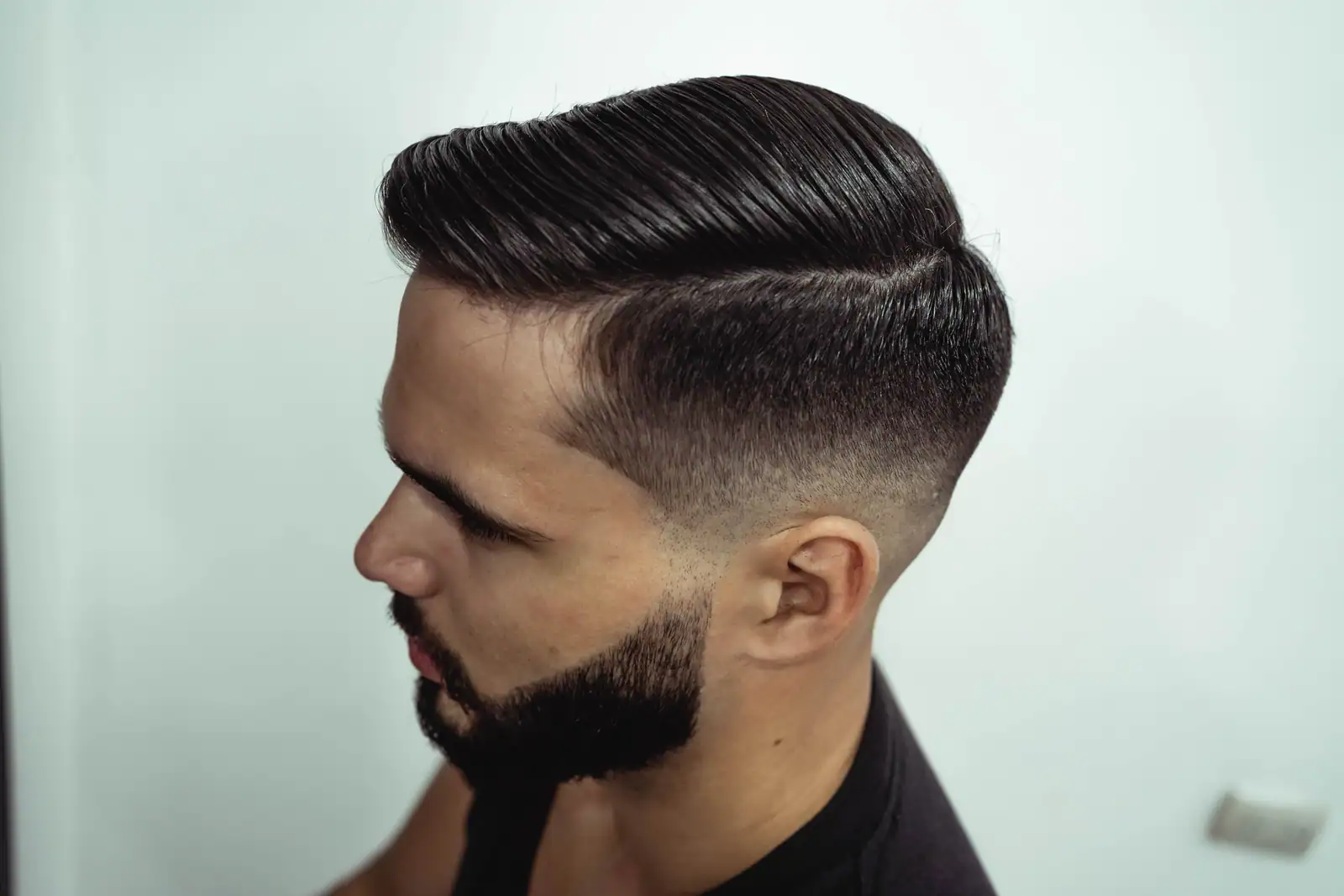 Homme de profil arborant une coupe nette avec dégradé sur les côtés et barbe taillée, sur fond clair