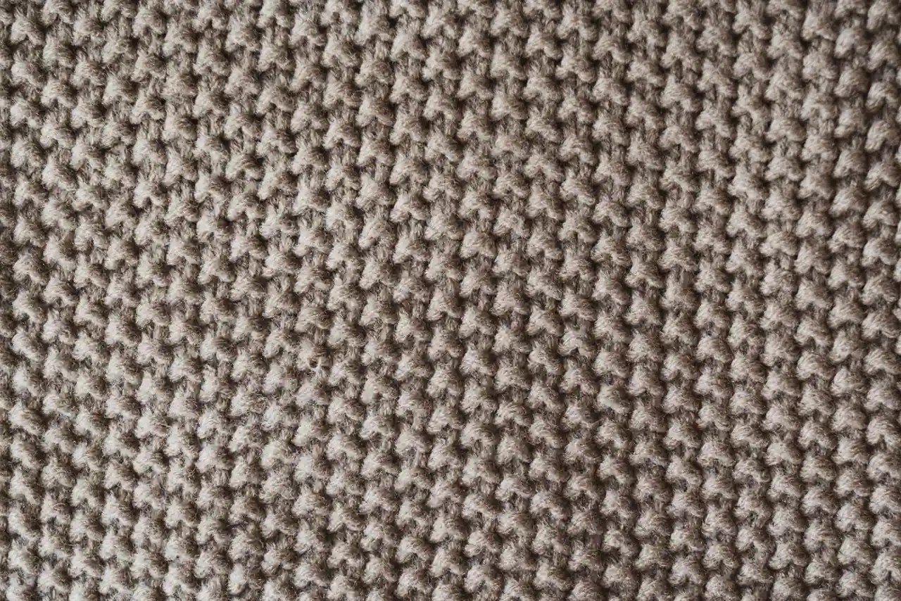 Gros plan d'un tricot de laine beige au point texturé, évoquant une écharpe tricotée à la main.