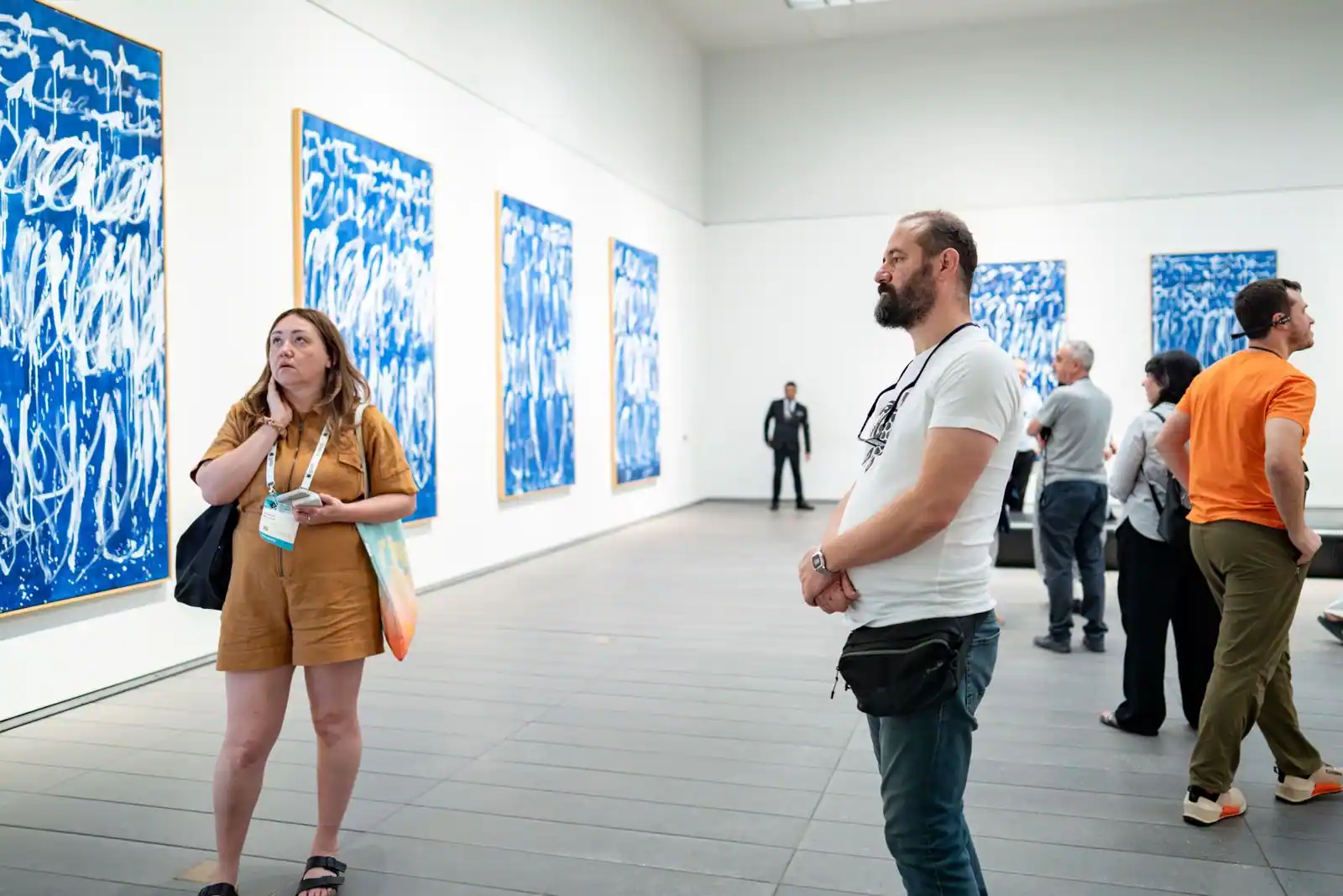 Salle d'exposition d'un musée aux grandes toiles abstraites bleues accrochées aux murs, observées par des visiteurs.
