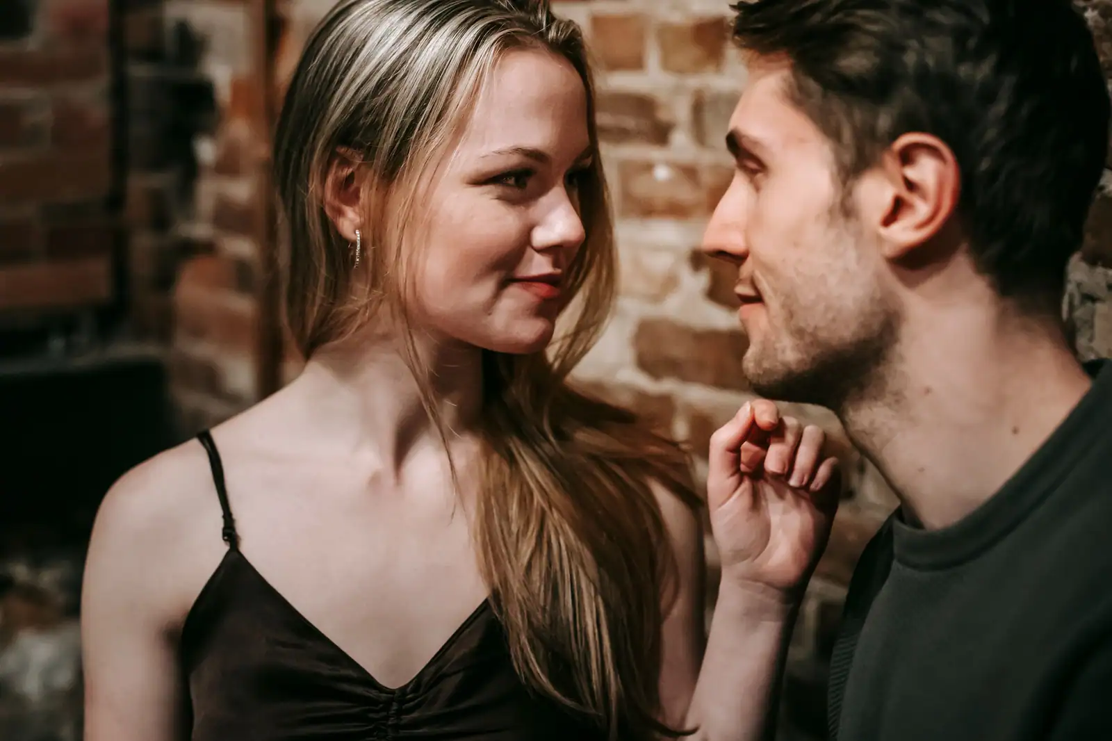 Un homme et une femme très proches se regardent dans les yeux en souriant, dans une ambiance tamisée et complice.