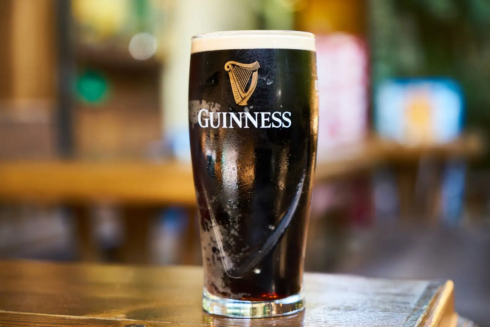 Pinte de stout Guinness à la mousse crémeuse, frappée du logo et de la harpe dorée, posée sur un comptoir de bois