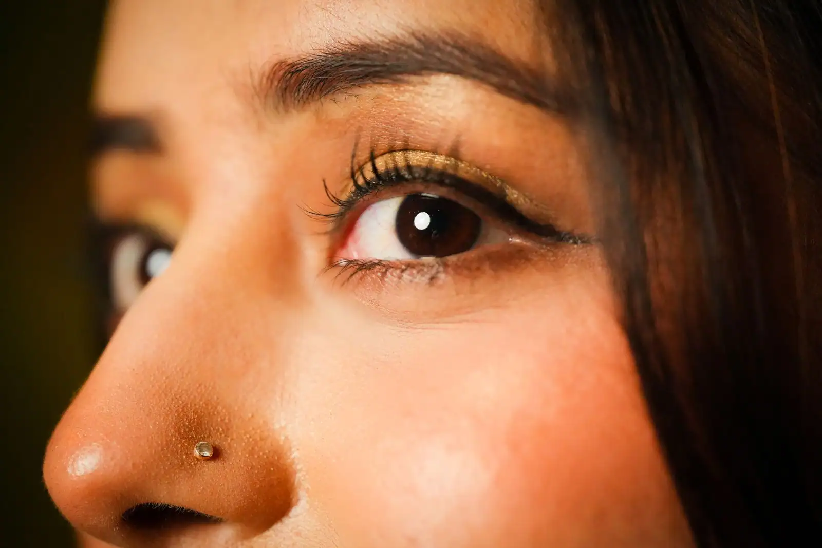 Gros plan d'un œil maquillé : eyeliner, fard à paupières doré et sourcil dessiné sur peau lumineuse