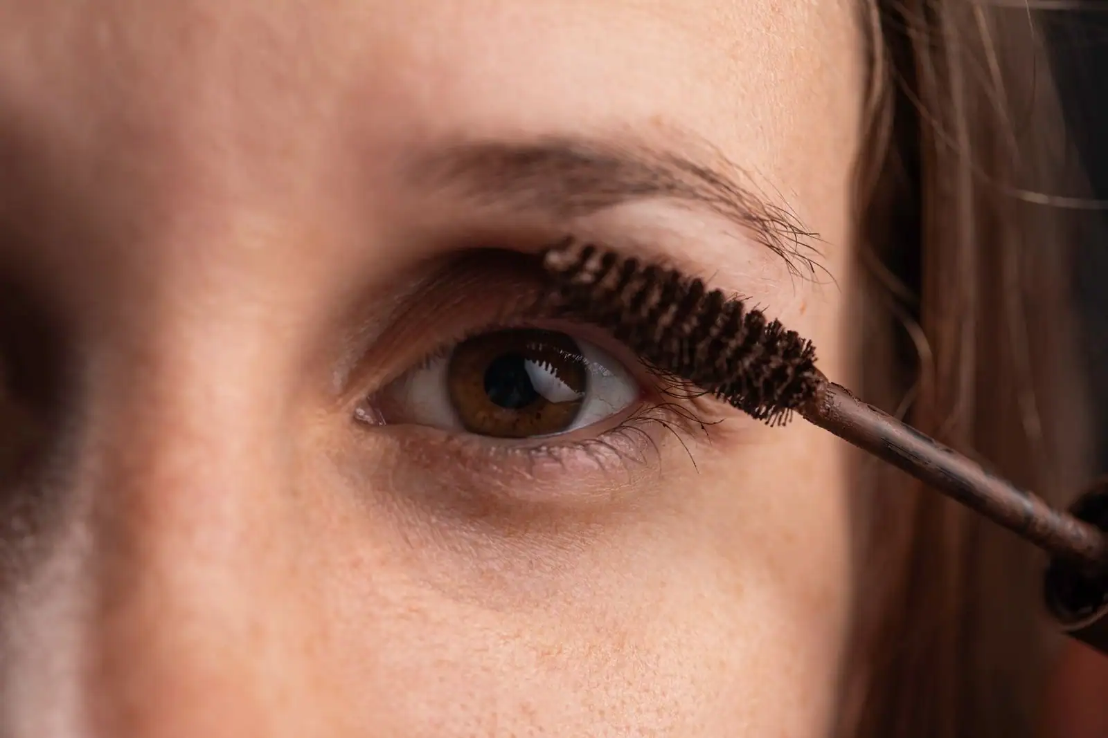 Gros plan d'un œil féminin pendant l'application du mascara à l'aide d'une brosse sur les cils