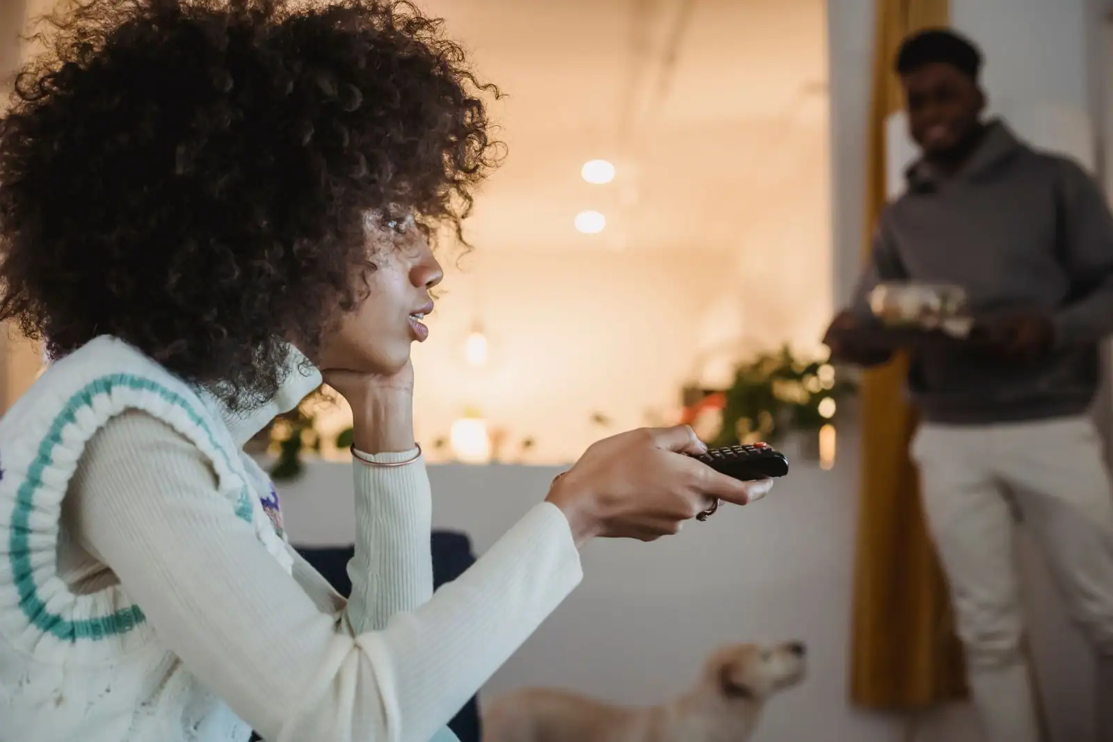 Femme tenant une télécommande, en train de regarder la télévision dans son salon