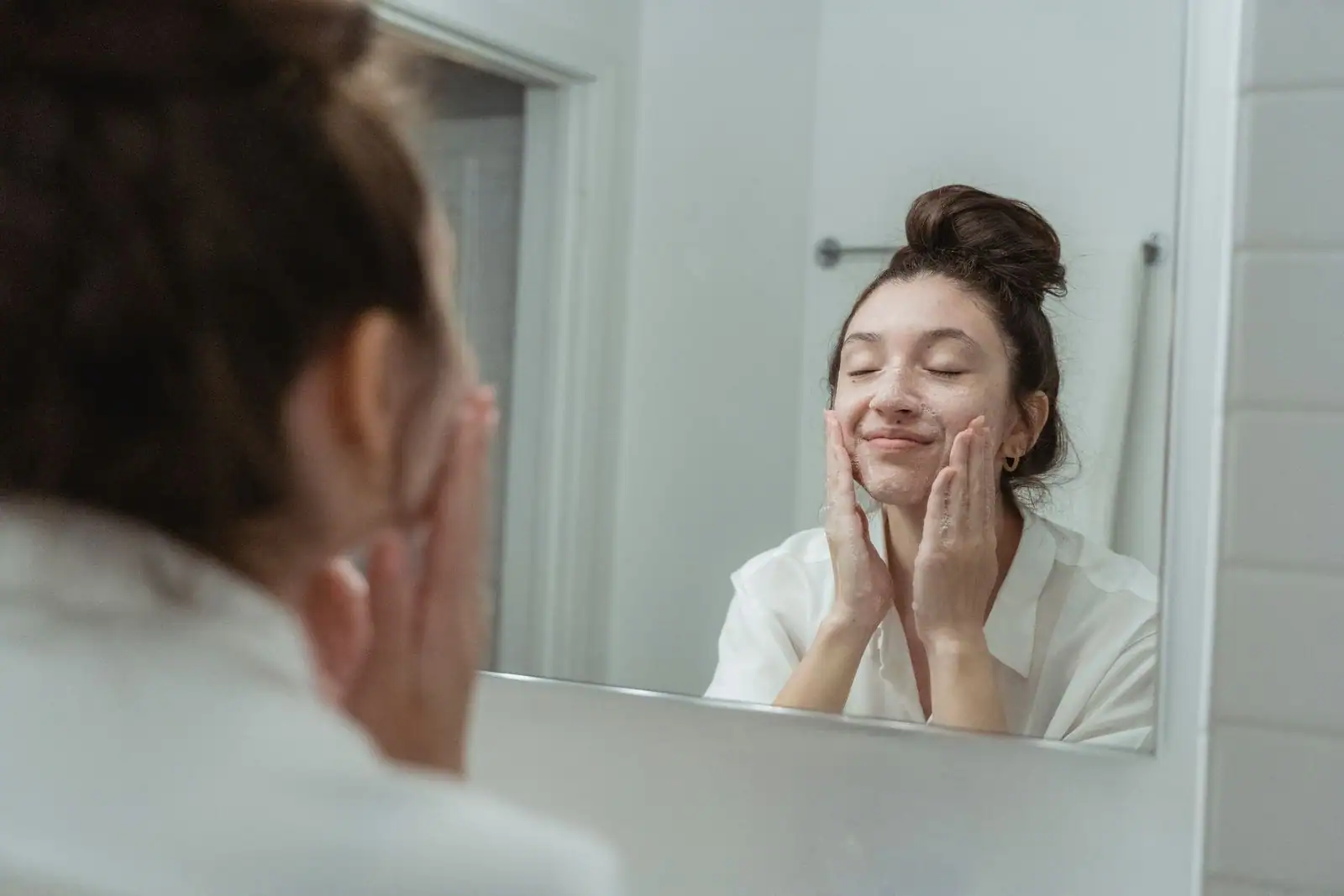 Femme se nettoyant le visage avec un nettoyant moussant au lavabo