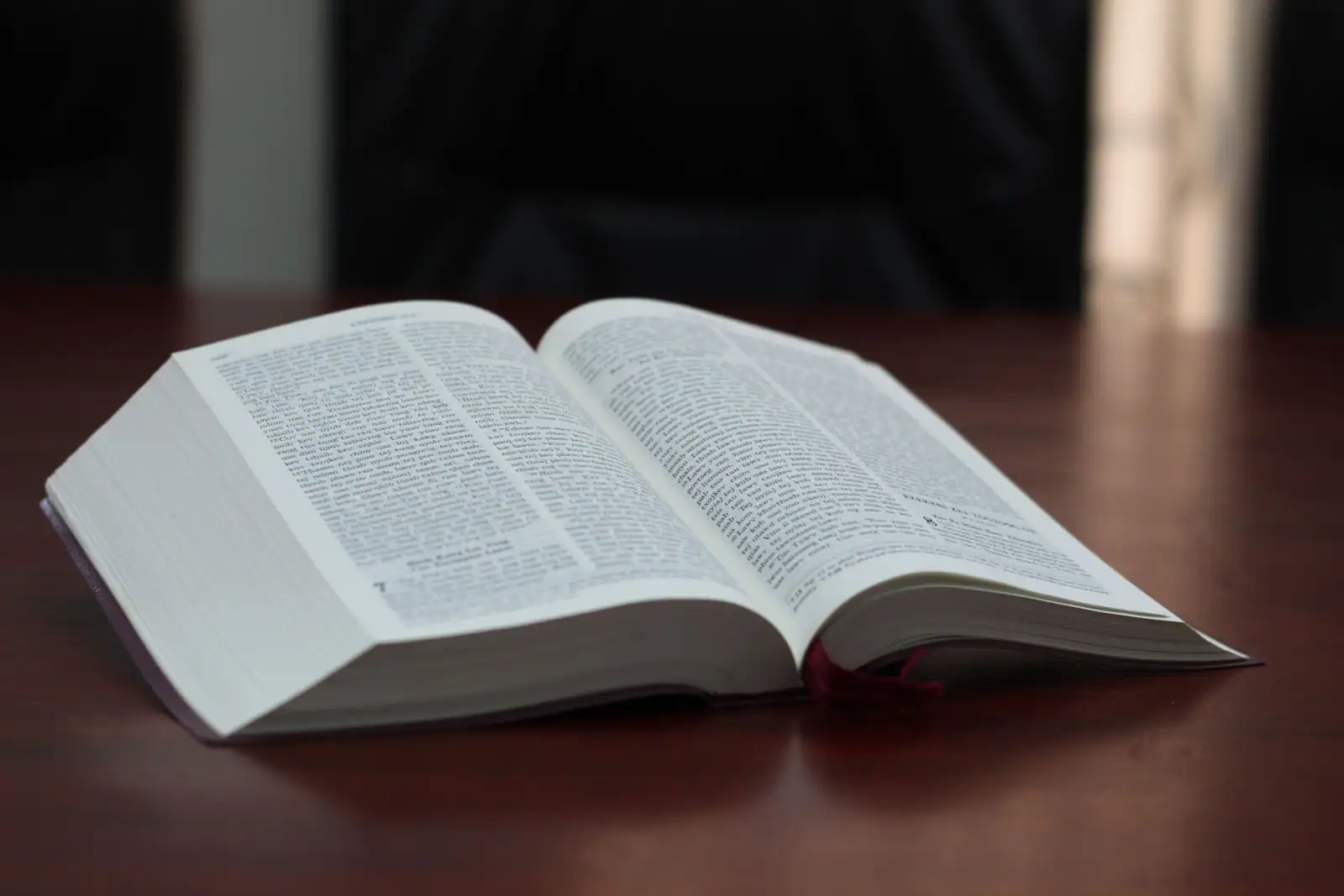 Bible ouverte posée sur une table en bois, pages éclairées par une lumière douce