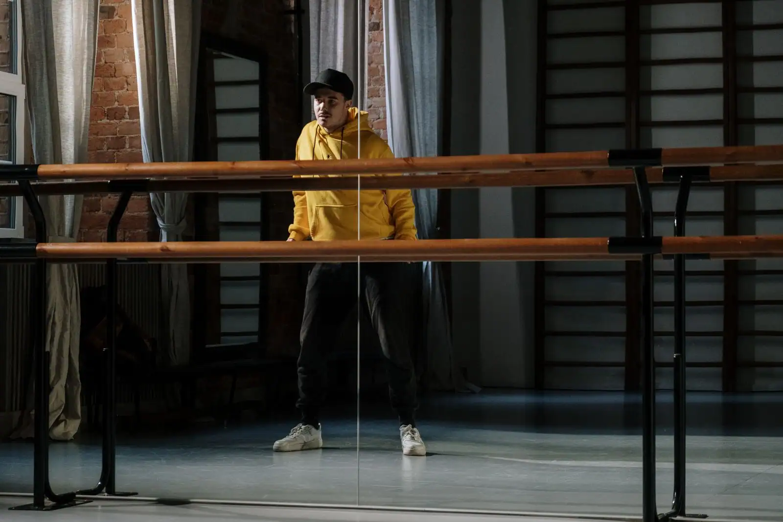 Jeune danseur de hip-hop en hoodie jaune et casquette, debout dans un studio de danse