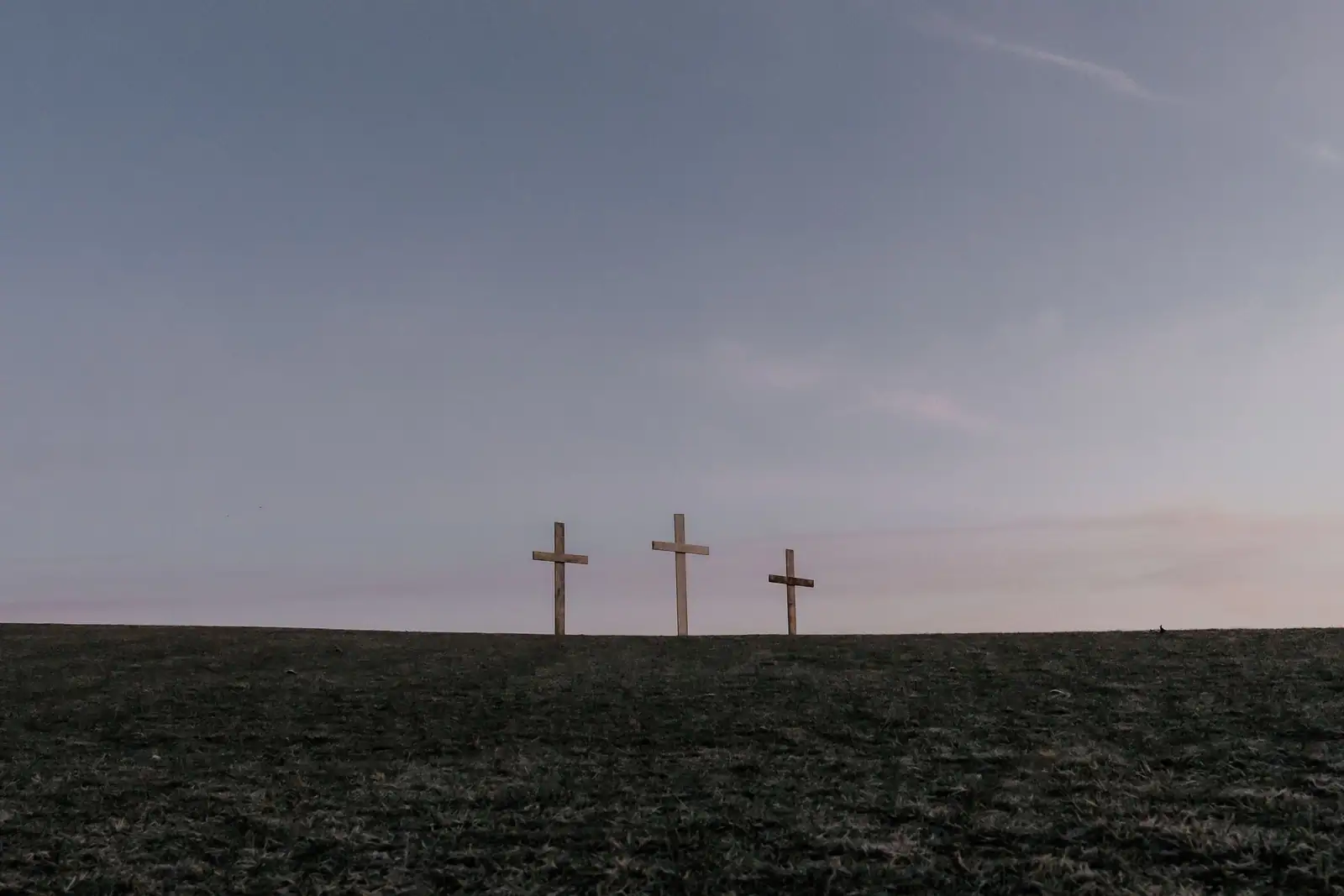 Trois croix dressées sur une colline au crépuscule, évoquant la scène du Calvaire