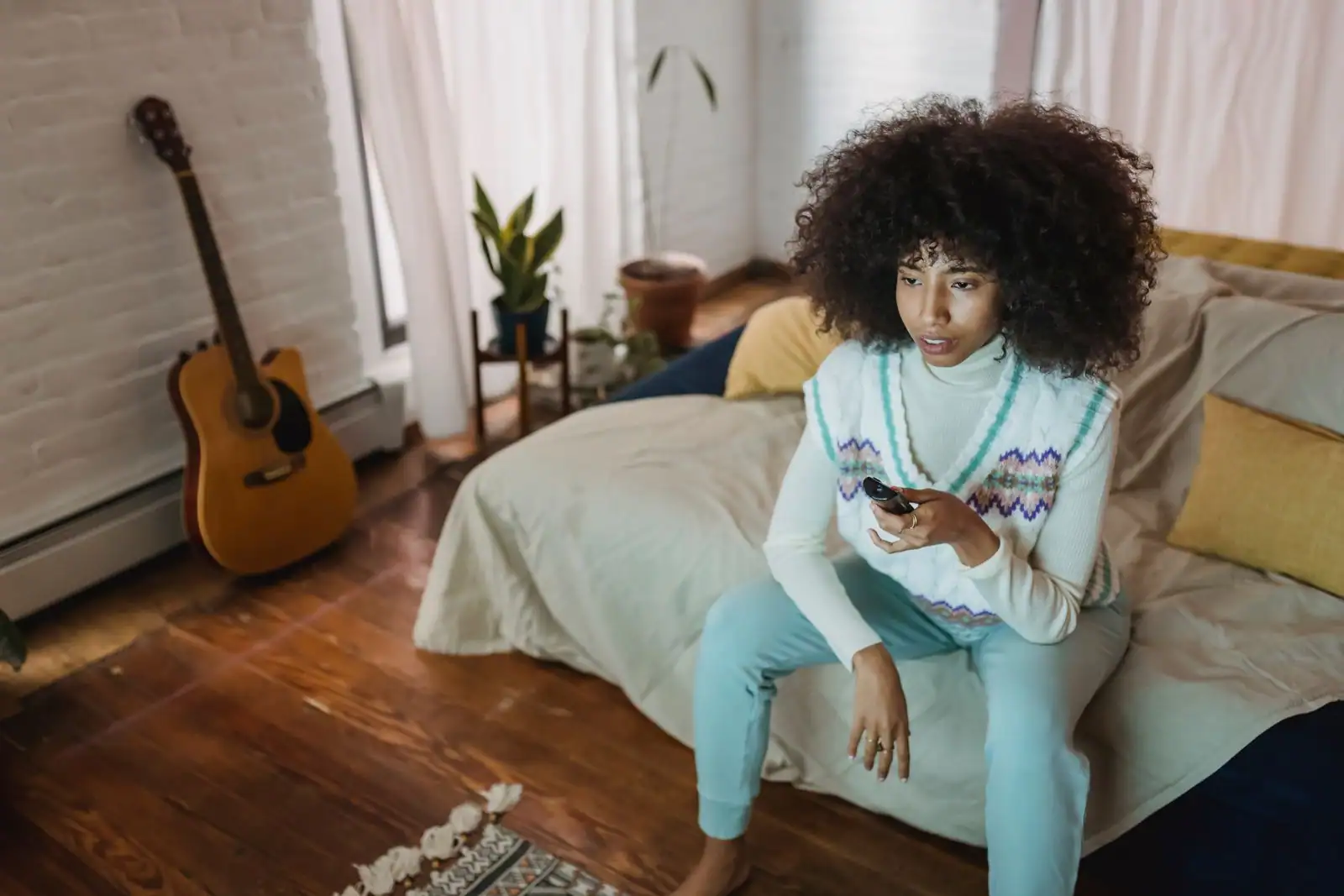 Une jeune femme assise chez elle, télécommande à la main, prête à choisir un programme à la télévision.