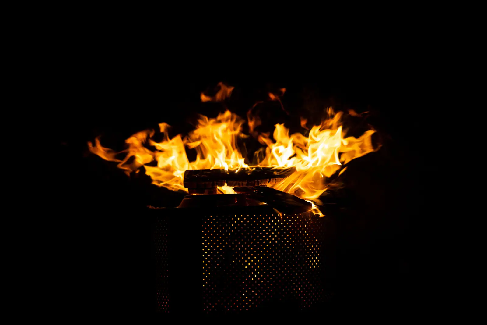 Flammes brûlant sur une vasque de métal sur fond sombre, évoquant un feu sacré