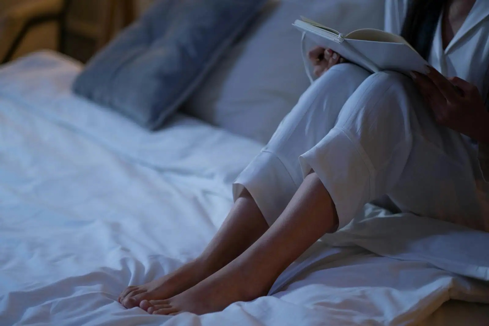Femme en pyjama assise sur un lit, lisant un livre dans la lumière douce du soir