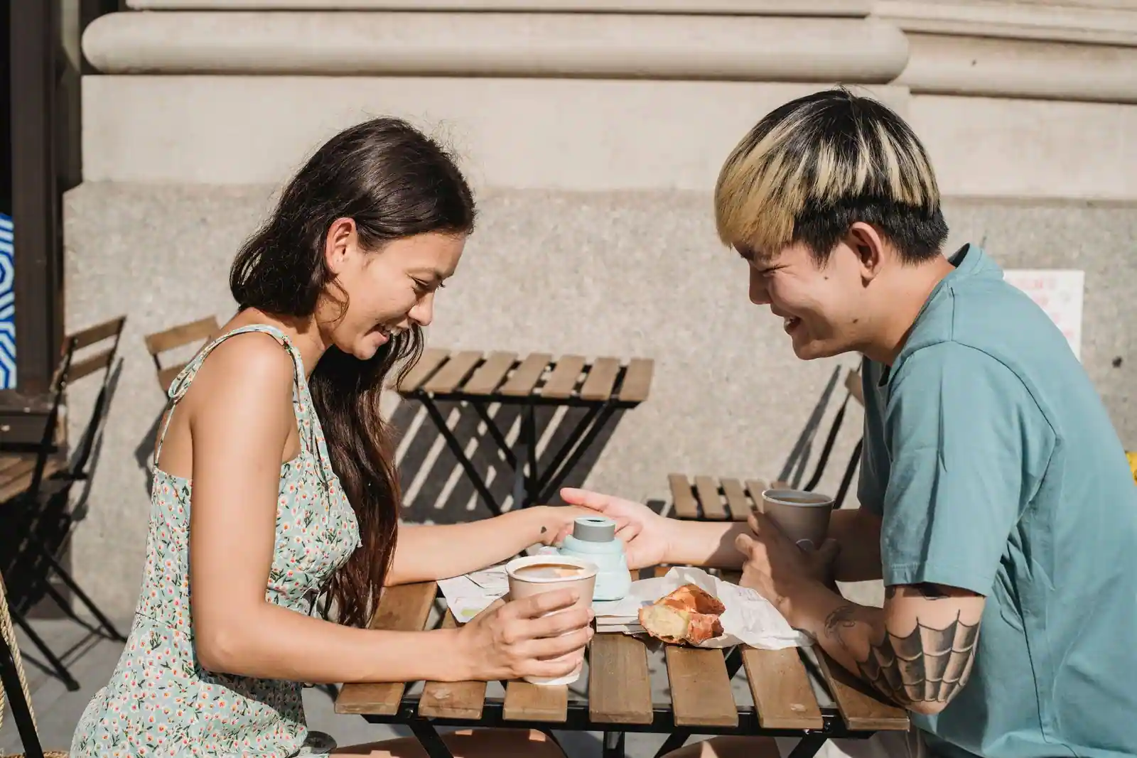 Jeune couple souriant partageant un café et une conversation en terrasse