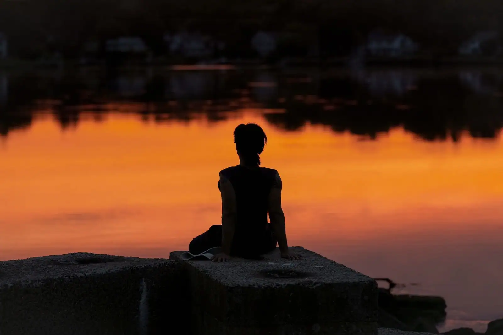Personne assise en contemplation au bord d’un lac au lever du soleil