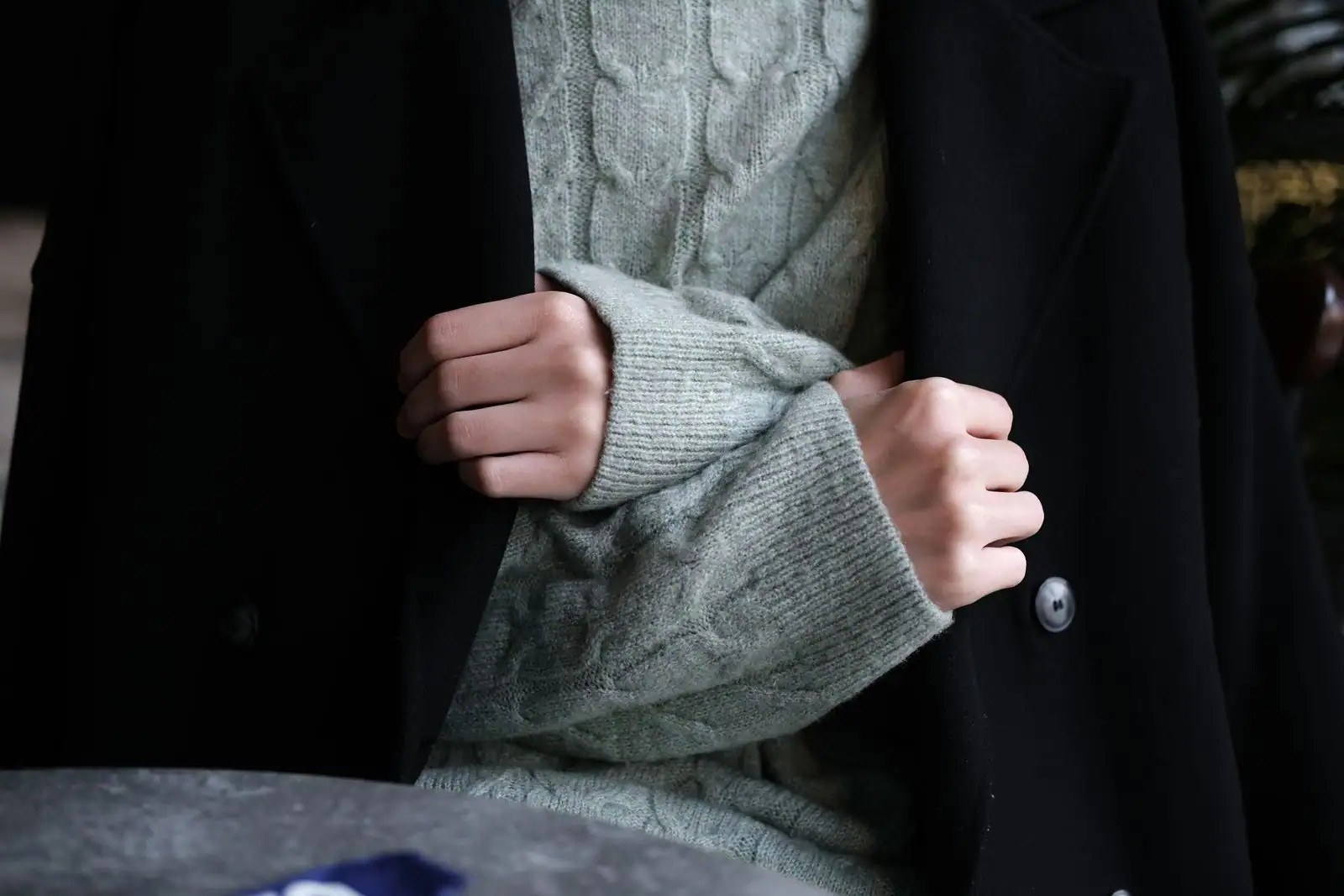 Femme en manteau long et grosse maille marchant dans une rue d'hiver aux tons neutres