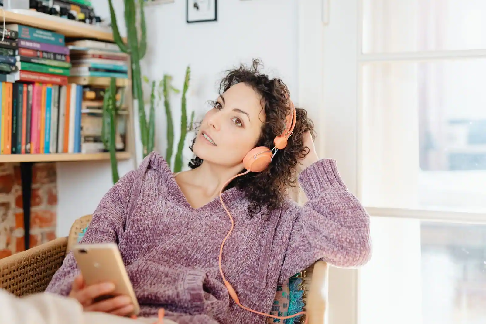 Jeune femme tenant un smartphone et écoutant de la musique au casque, installée dans un intérieur cosy