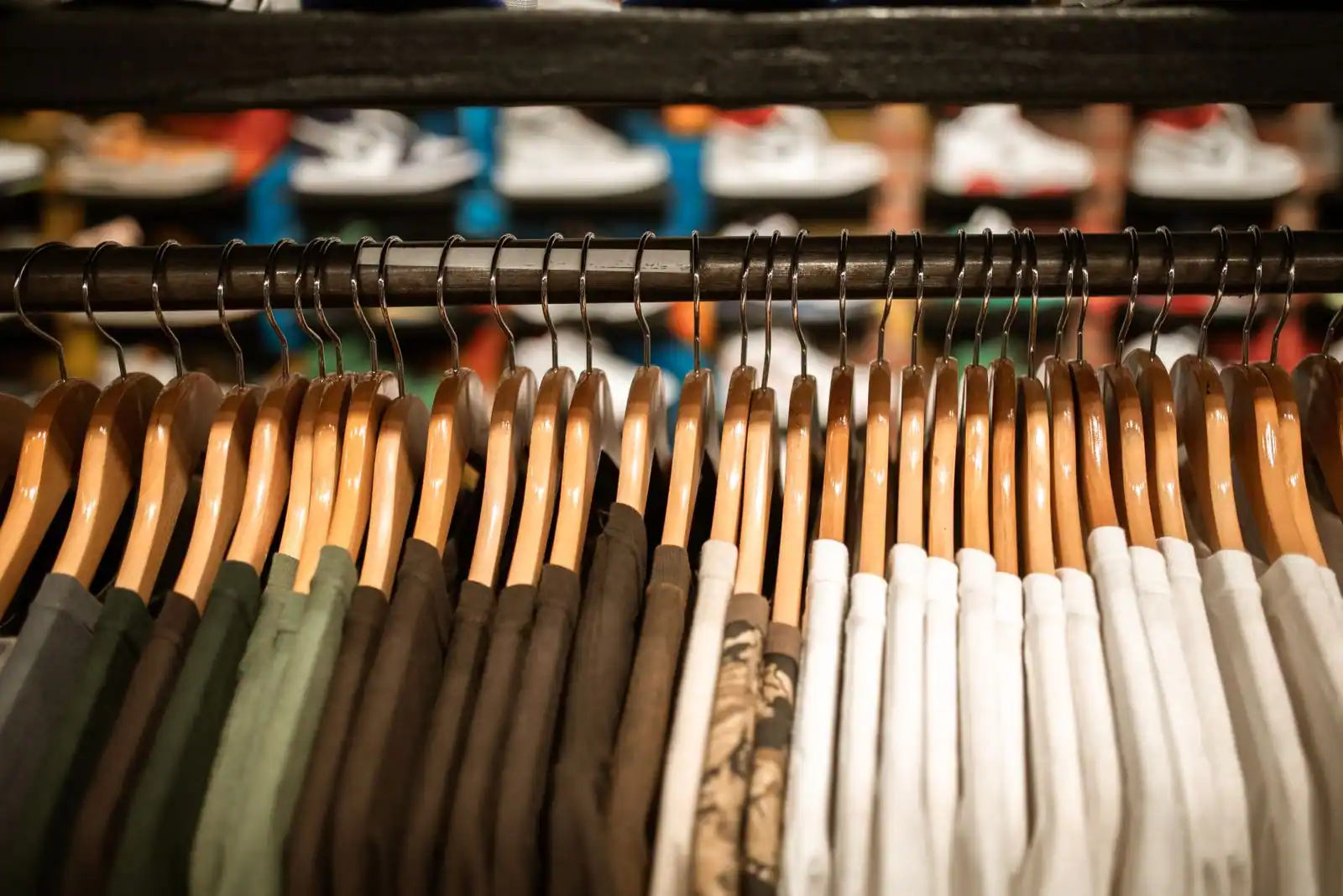 Vêtements sur cintres en bois alignés sur une tringle, étagère de baskets en arrière-plan
