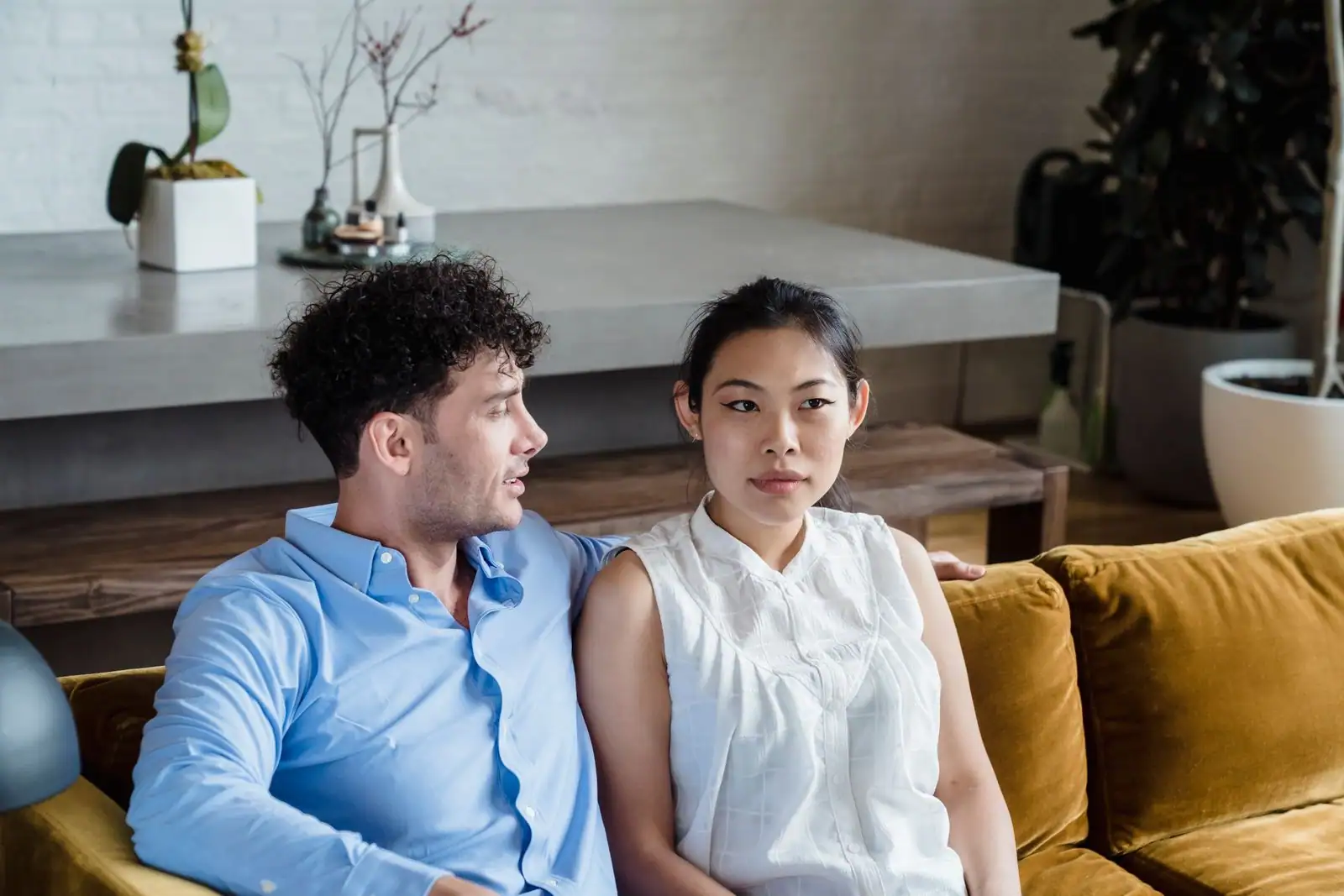 Un couple assis sur un canapé dans son salon, lui parle tandis qu'elle paraît pensive et préoccupée