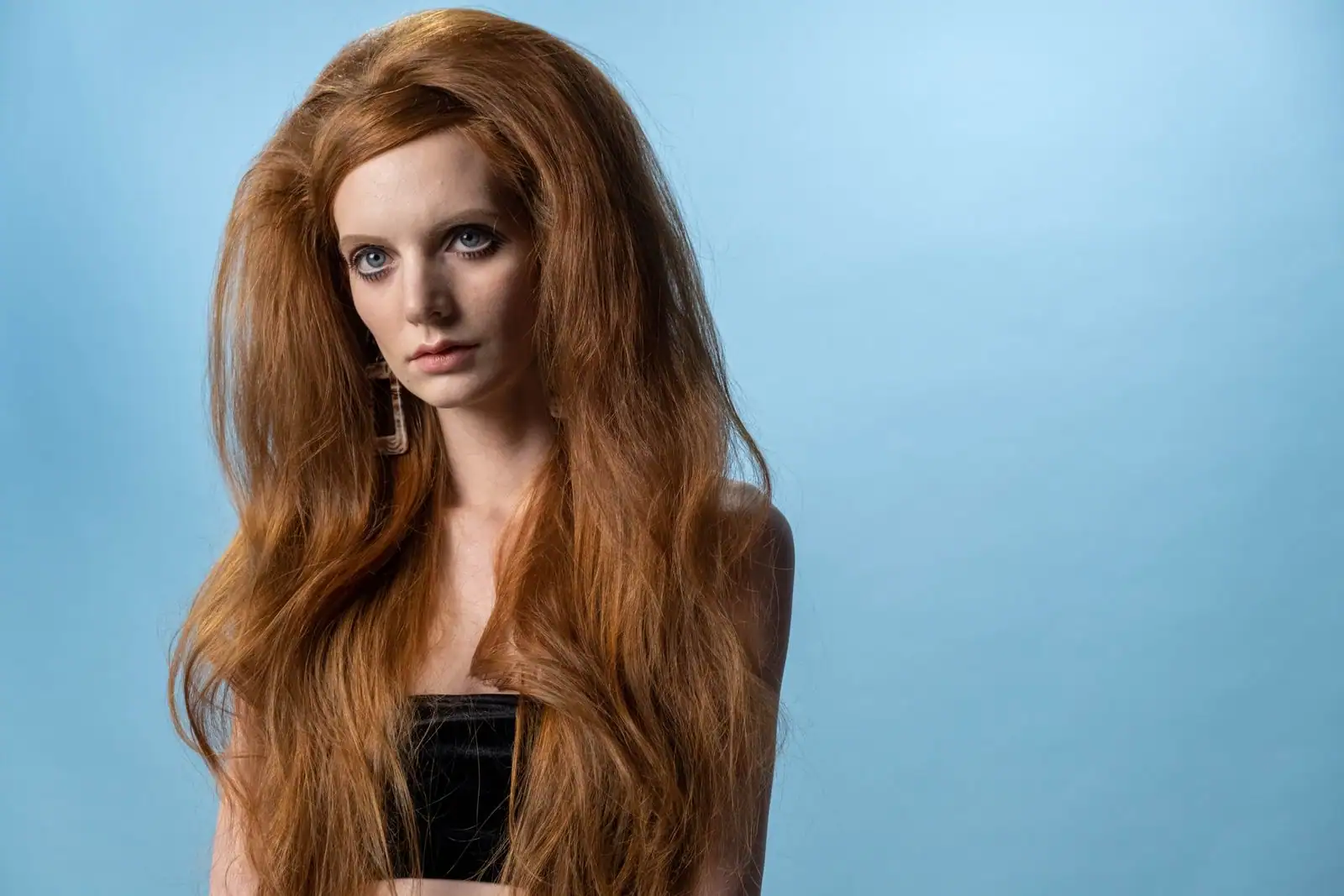 Femme aux longs cheveux épais et volumineux d'un roux cuivré, mis en valeur devant un fond bleu clair.