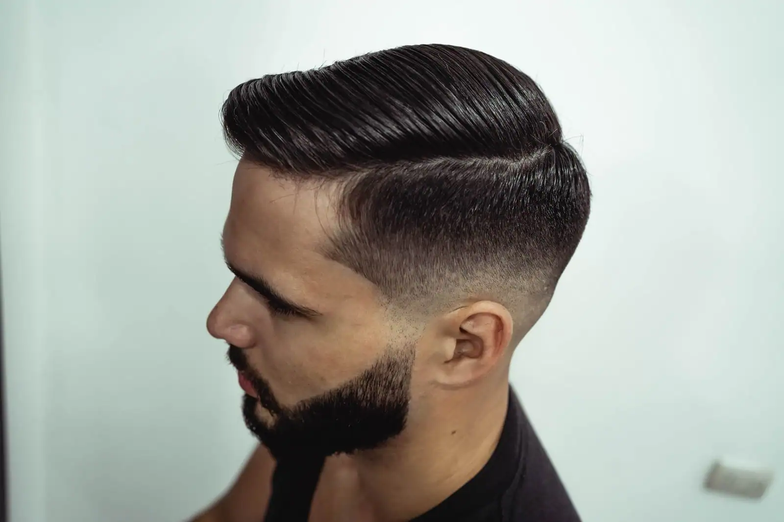 Un homme de profil arbore une coupe moderne, raie sur le côté et côtés dégradés, avec une barbe soignée
