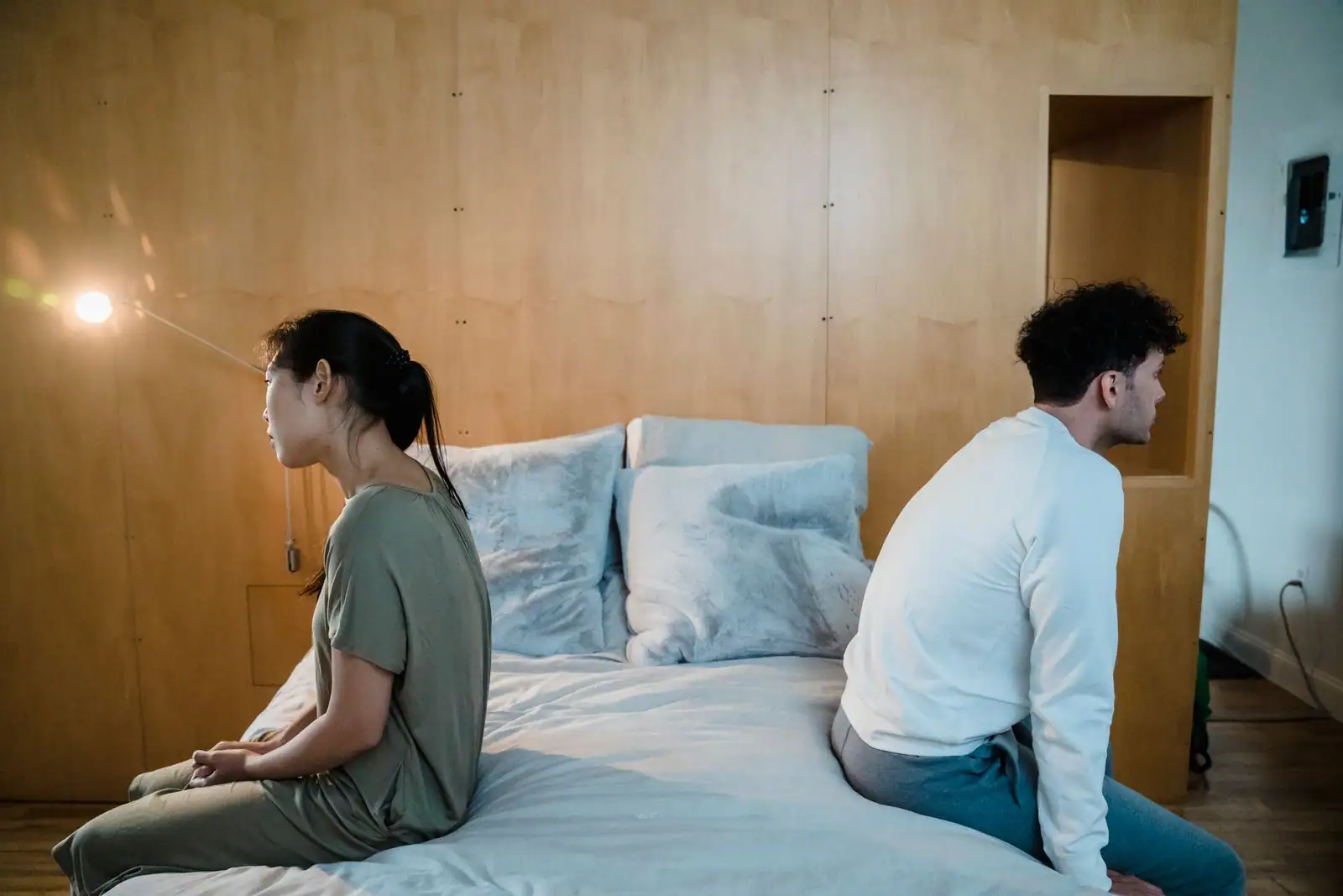 Un couple assis dos à dos sur les bords opposés d un lit, l air pensif, évoquant une tension dans la relation