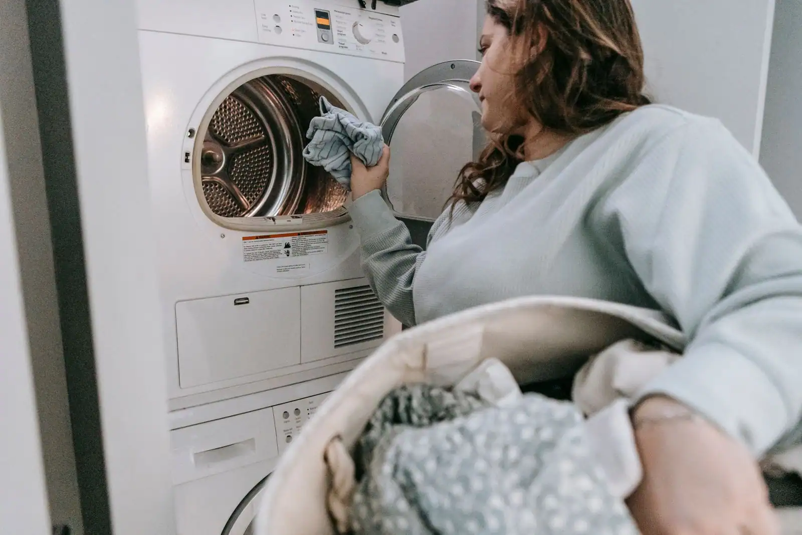 Une femme place du linge dans une machine à laver, un panier de vêtements à la main, dans une buanderie
