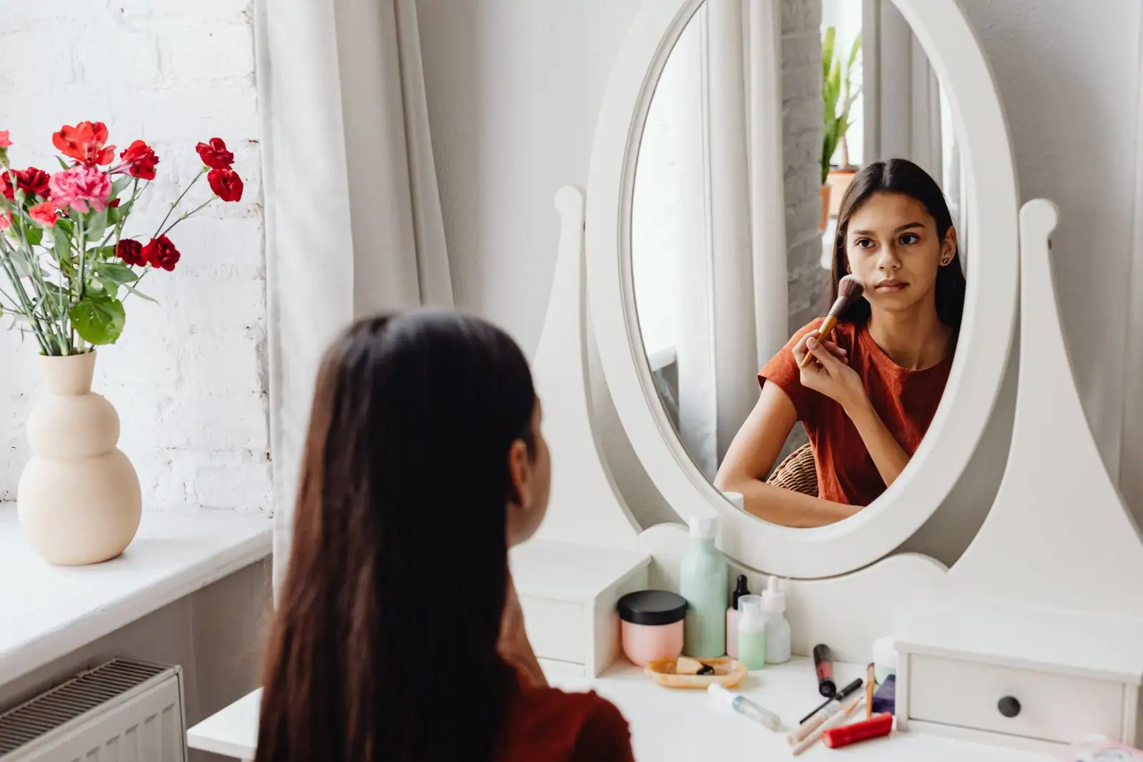 Une femme applique un maquillage naturel devant un miroir de coiffeuse, un pinceau à la main