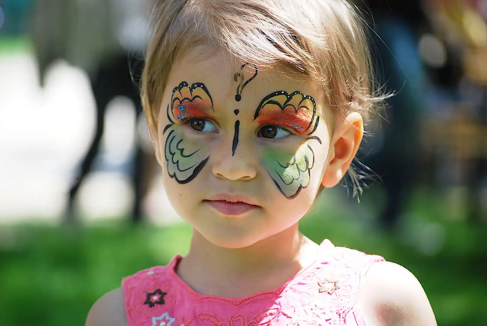 Fillette au maquillage papillon peint autour des yeux, ailes colorées orange et vert soulignées de noir.