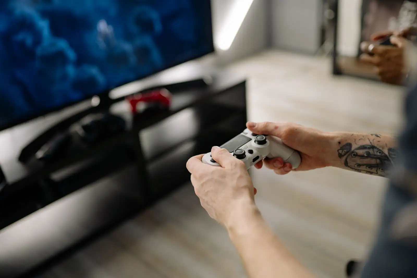 Mains tenant une manette de jeu vidéo blanche devant un téléviseur, dans le salon, pendant une partie.