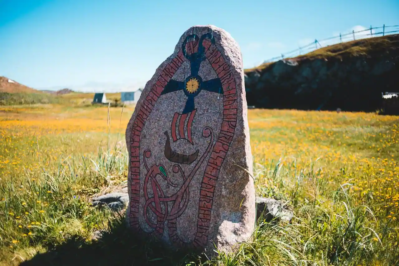 Une pierre runique viking peinte, gravée de runes et d'un drakkar, dressée dans une prairie scandinave.
