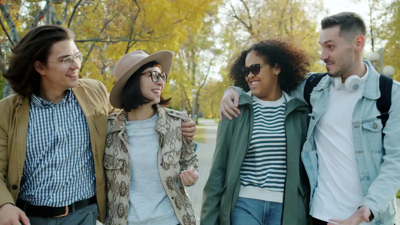 Quatre amis marchent ensemble et discutent dans un parc aux couleurs d'automne, un jour de sortie
