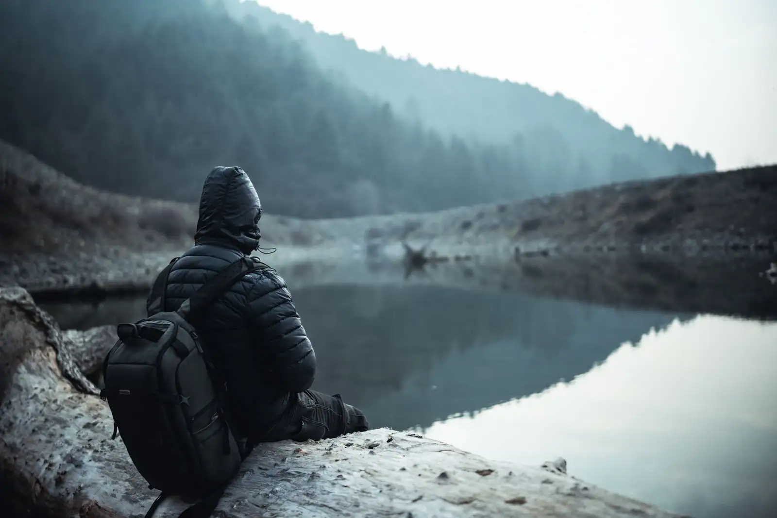 Une personne assise au bord d'un lac brumeux, dans un moment de calme et de contemplation en pleine nature.