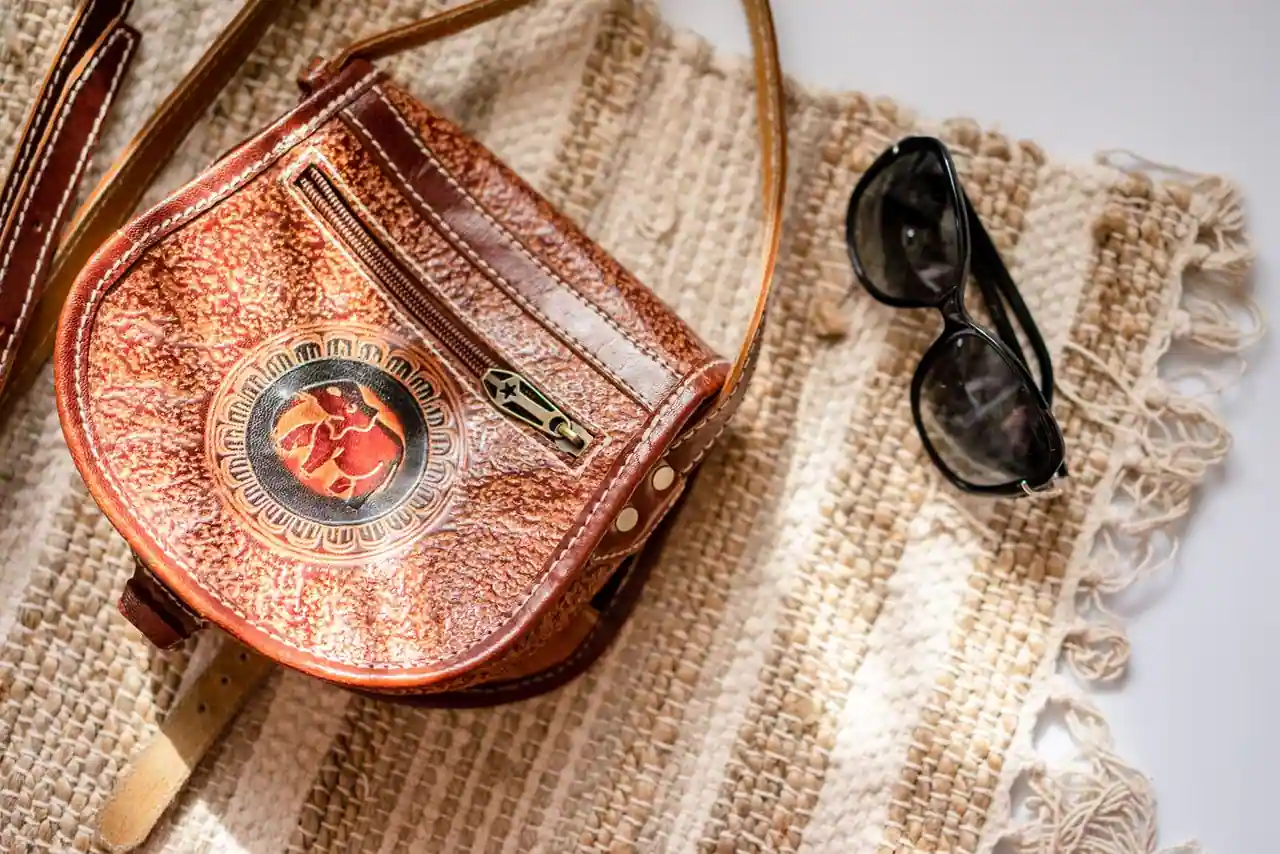 Sac en cuir ouvragé et lunettes de soleil posés sur un tissu tissé, composition d'accessoires.