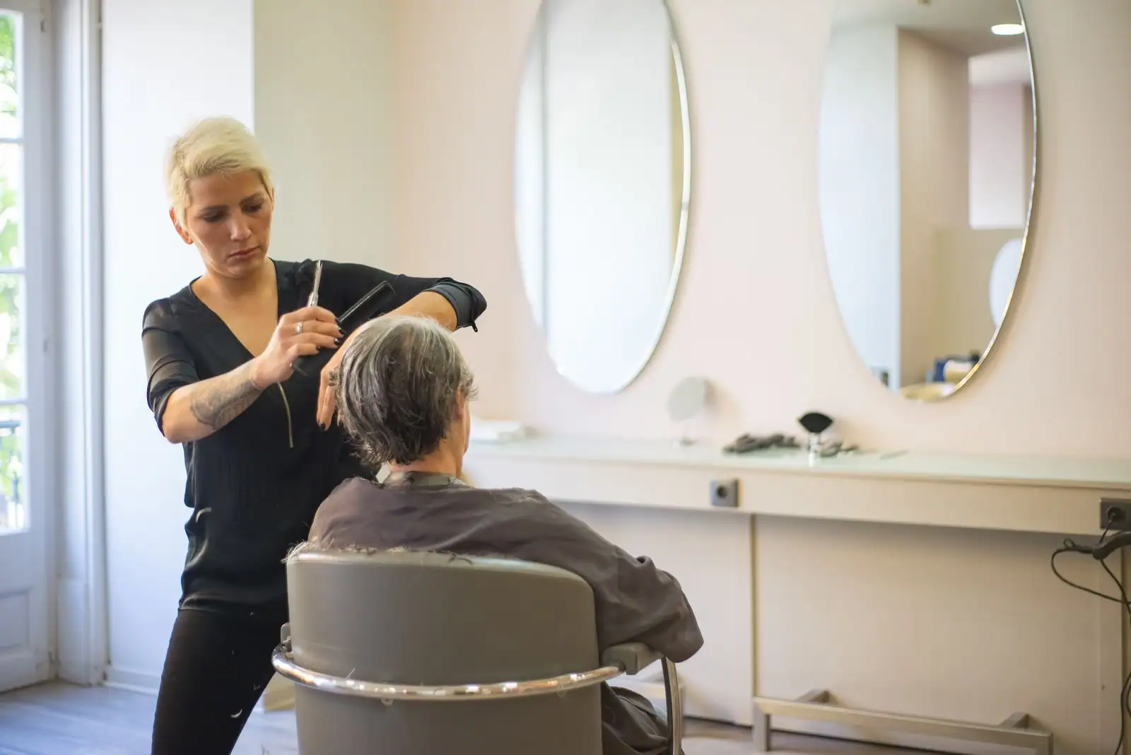 Coiffeuse professionnelle coupant les cheveux d'une cliente dans un salon de coiffure lumineux