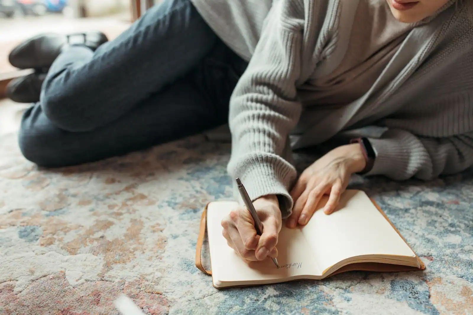 Personne assise seule près d'une fenêtre, carnet ouvert sur les genoux, dans une lumière douce en fin de journée