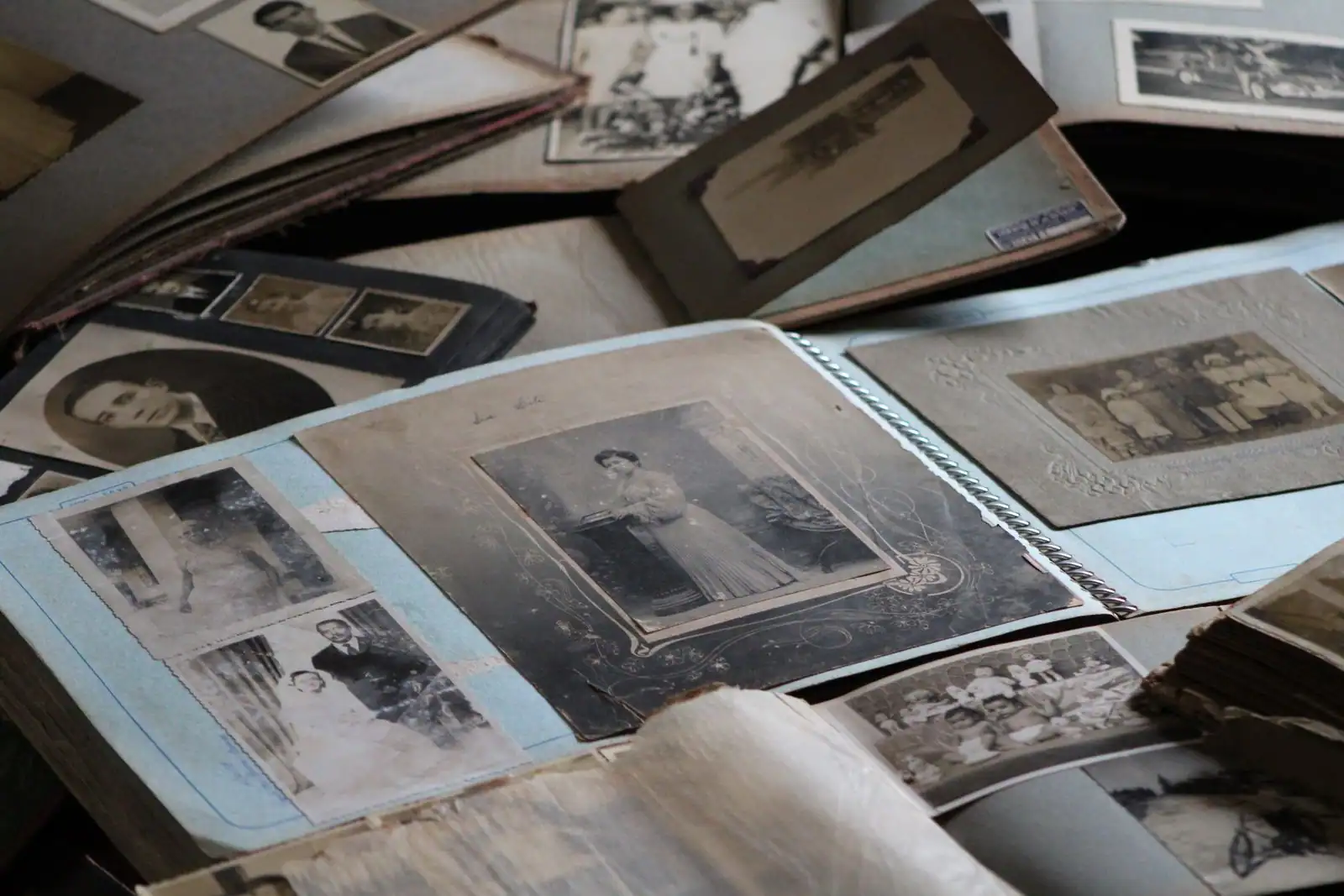 Albums de photographies de famille anciennes, entassés et feuilletés, portraits en noir et blanc.