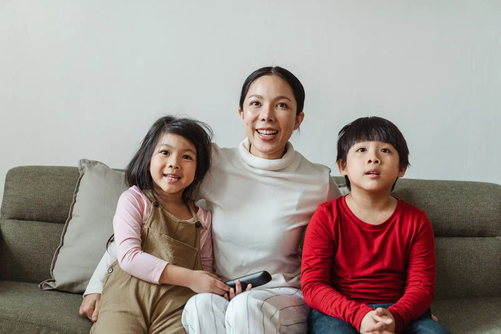 Mère souriante entre ses deux enfants, installés sur le canapé pour regarder un film ensemble.