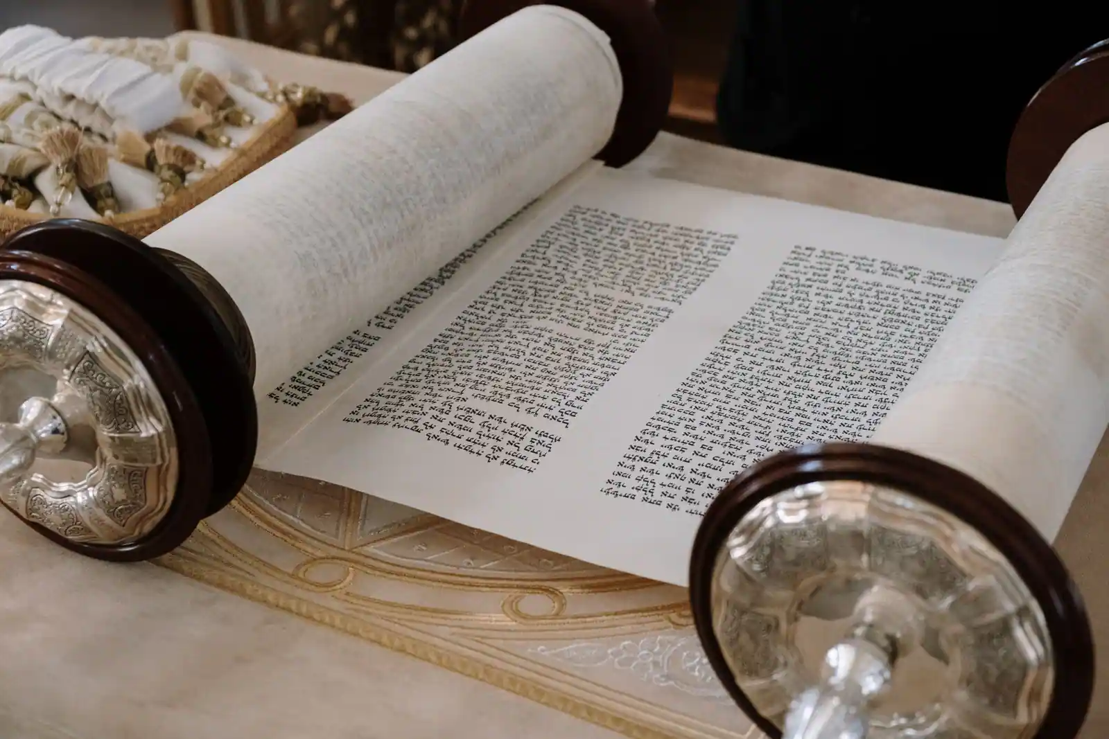 Rouleau de la Torah ouvert, texte hébraïque manuscrit visible, posé sur une table de synagogue.