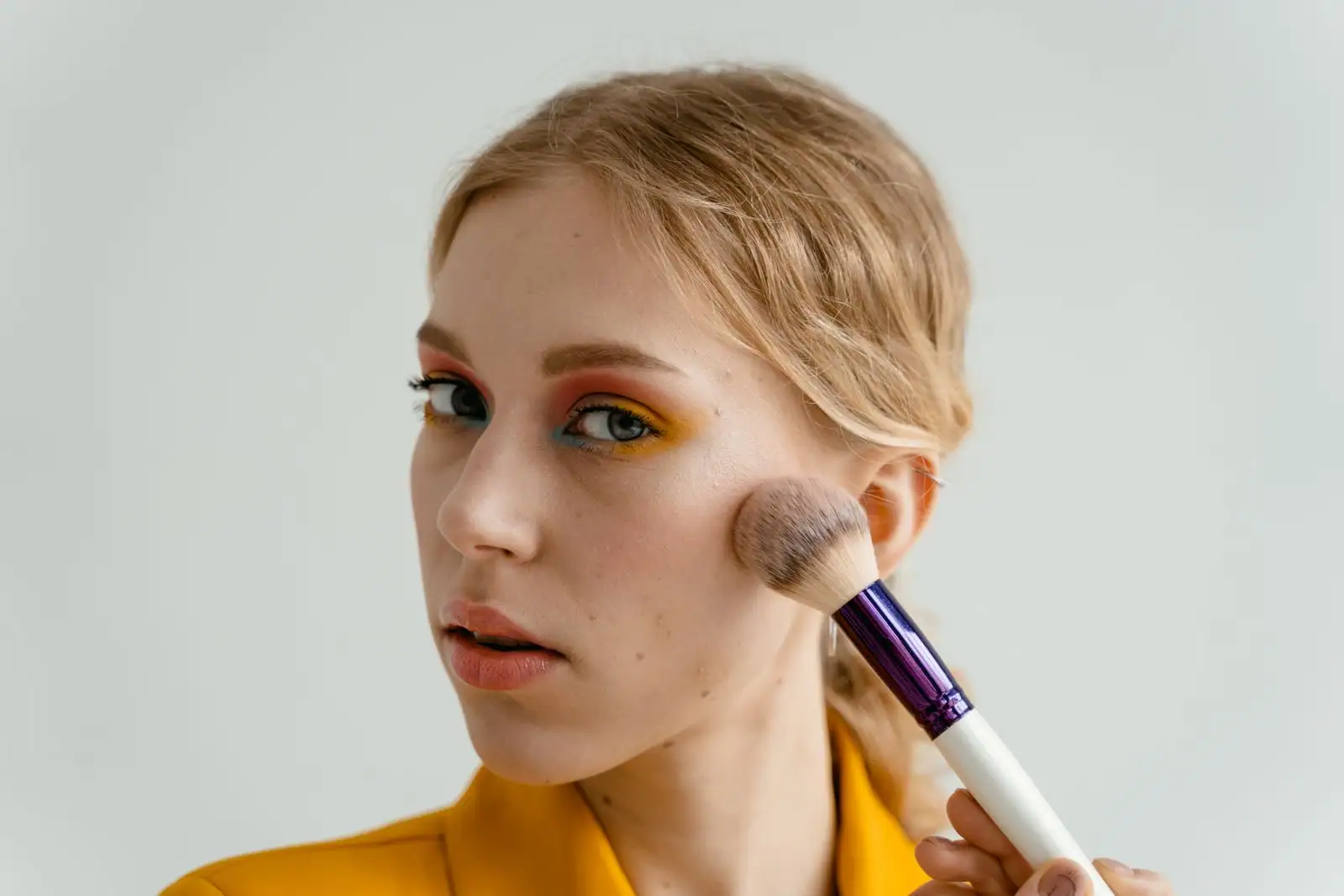 Fard à paupières bleu vif et blush rose appliqués sur une pommette, maquillage rétro coloré