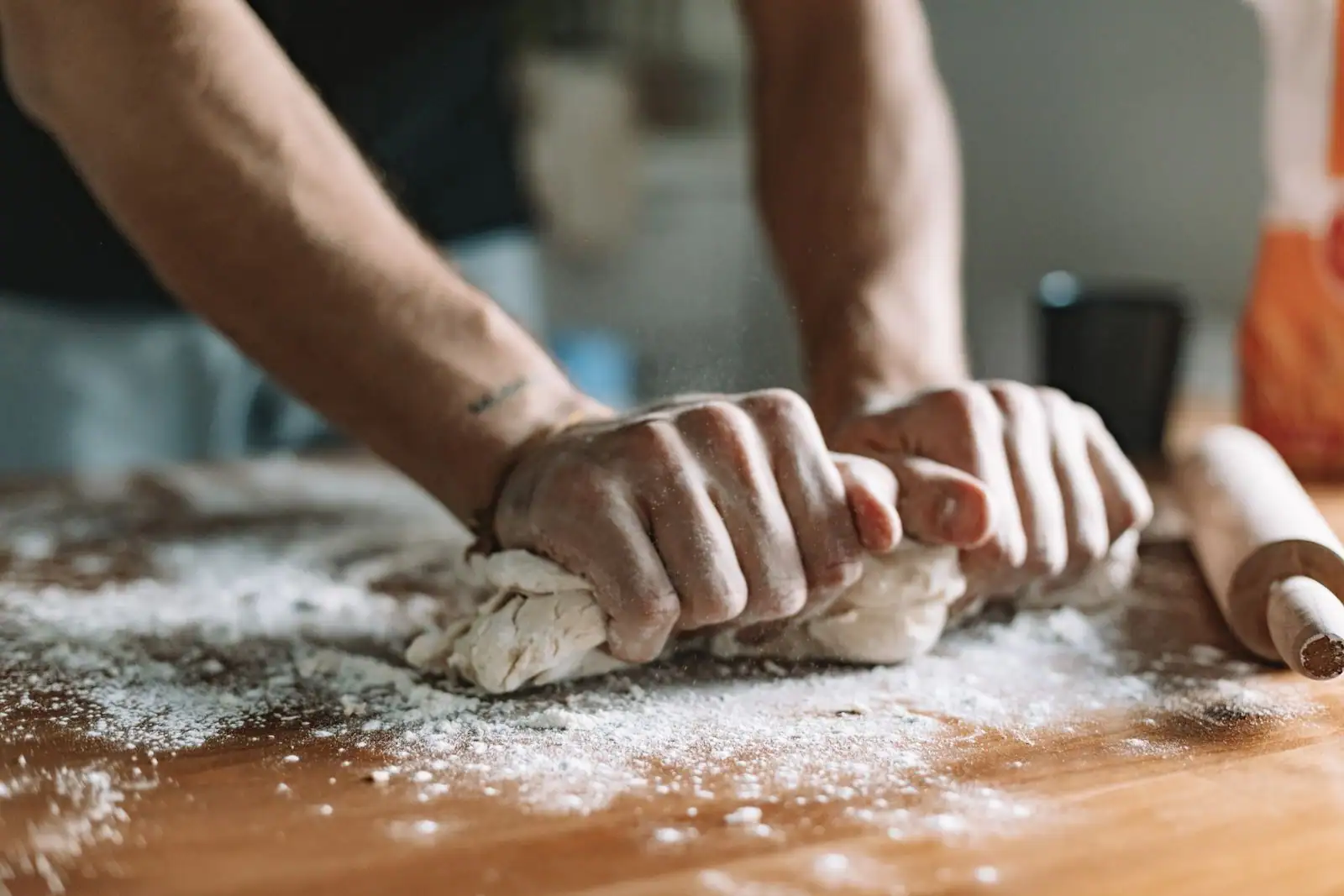 Des mains pétrissent une pâte traditionnelle sur un plan de travail en bois, dans une cuisine familiale