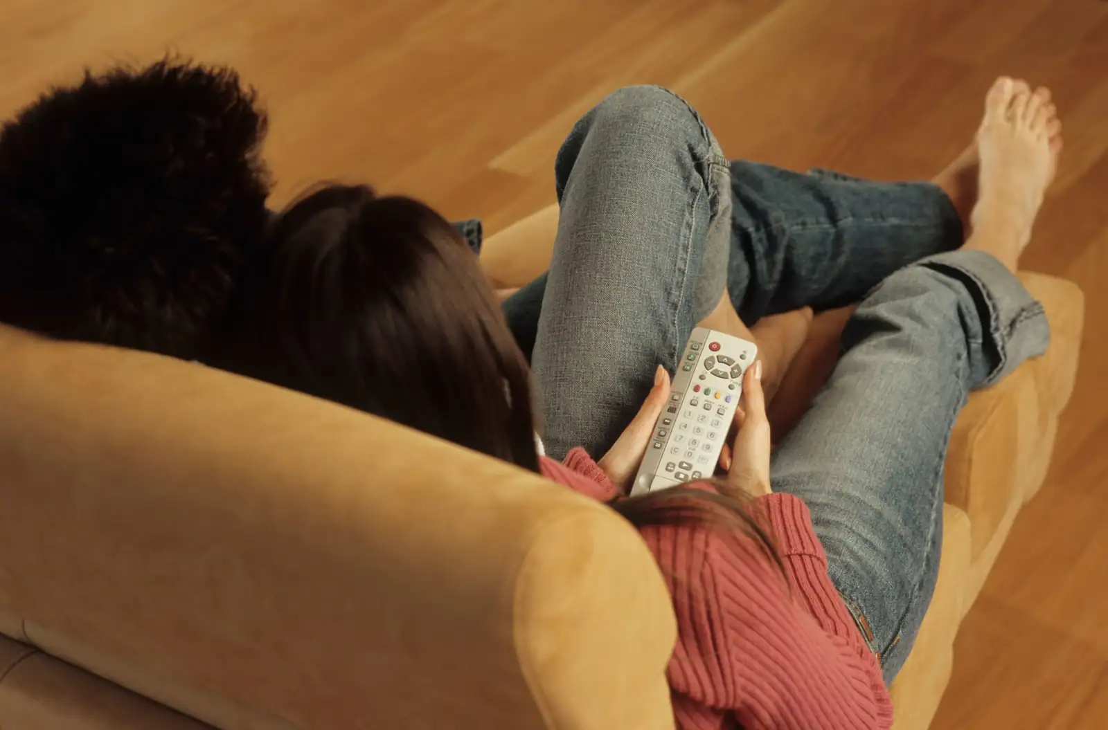 Couple installé dans un canapé le soir, télécommande en main devant la télévision